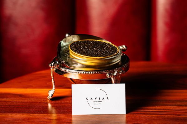 Elegant caviar tin on a silver stand with a Caviar Concierge card on a wooden table.