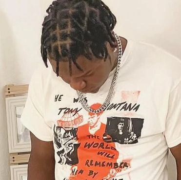 Man with braided hair wearing a white Tupac Shakur graphic t-shirt and a silver chain.
