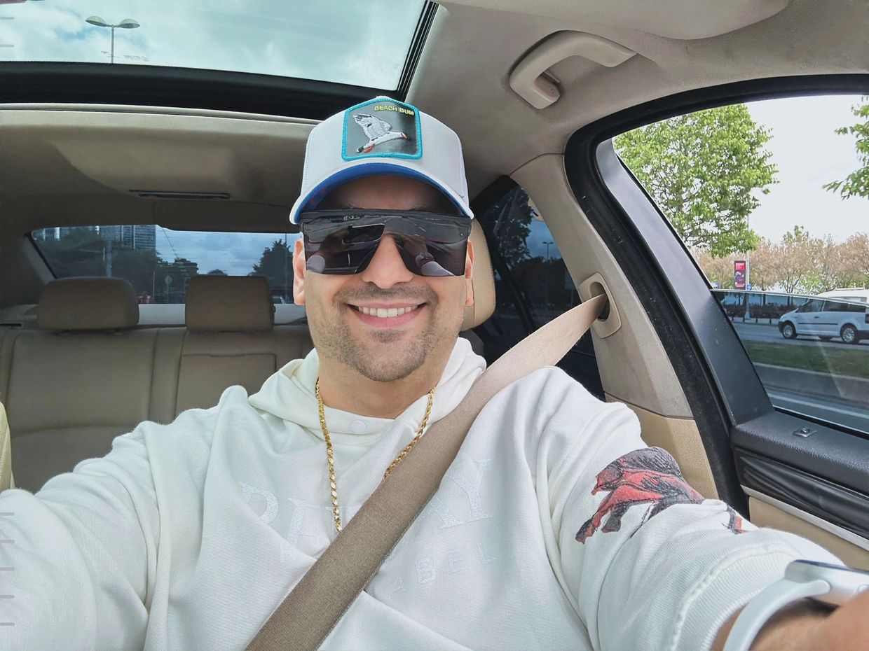 Man wearing sunglasses and a cap smiling inside a car.