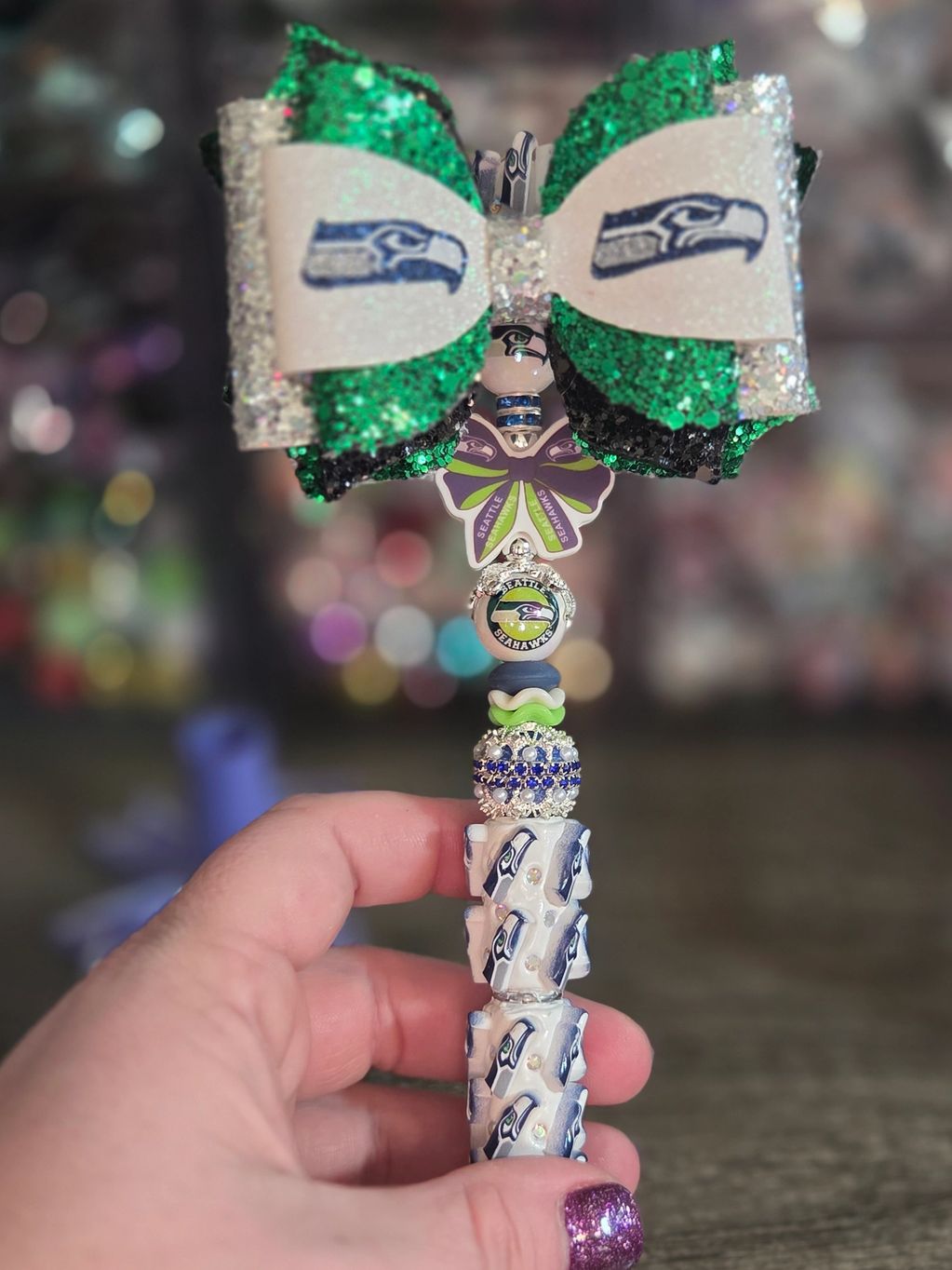 Hand holding a Seattle Seahawks-themed beaded ornament with a glittery bow.