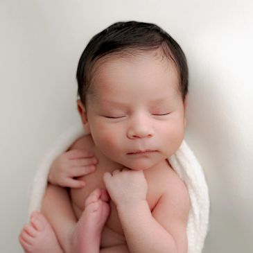 Peaceful newborn baby sleeping wrapped in white blanket.