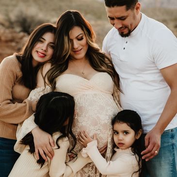 Family embracing pregnant mother outdoors.