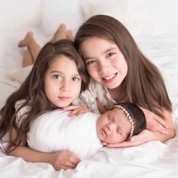 Three siblings, two girls and a newborn baby, posing together.