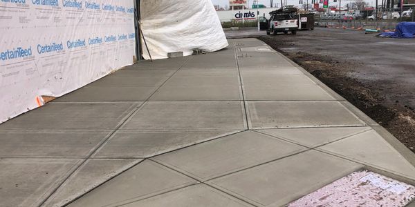 Newly poured concrete sidewalk with geometric patterns near construction site.
