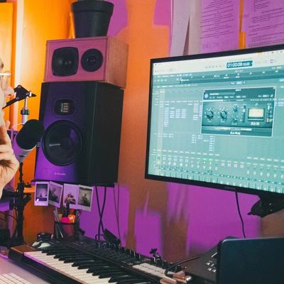 Person working in a music studio with keyboard and speakers.