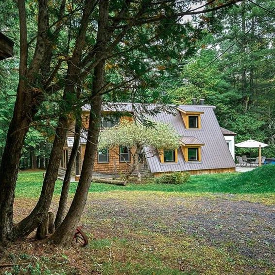 A cozy cabin with a sloped metal roof surrounded by lush green trees.