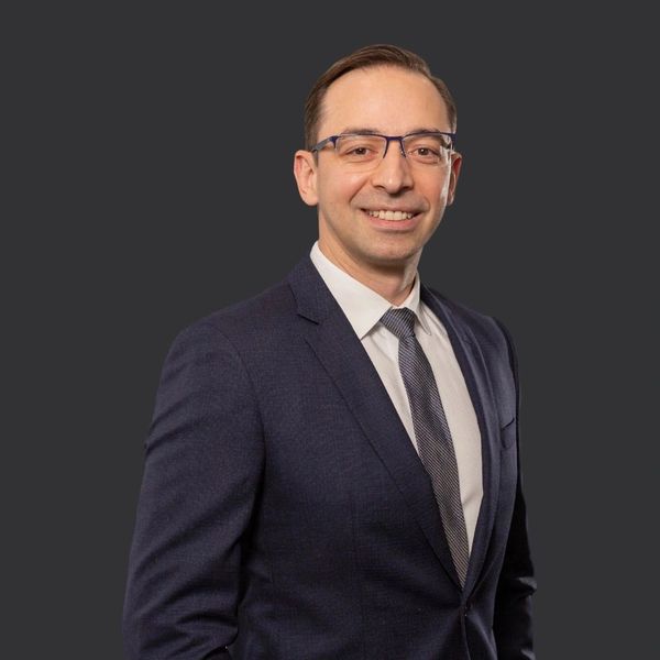 Man in a dark suit and glasses smiling.