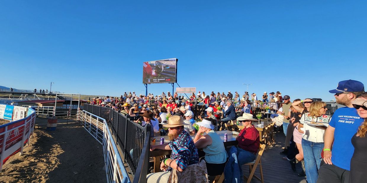 Crowd watches an outdoor rodeo event under clear blue skies.