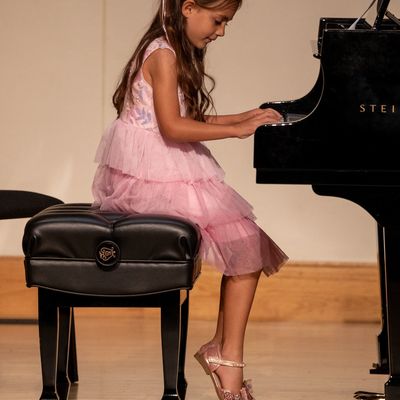Young girl in a pink dress playing a grand piano with focus.