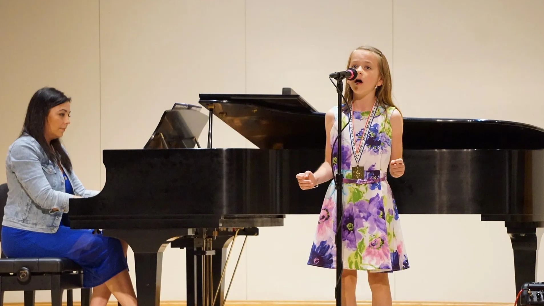 A young girl singing with a pianist accompanist.
