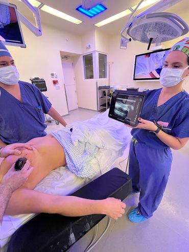 Medical professionals performing an ultrasound on a patient's arm in a clinical setting.