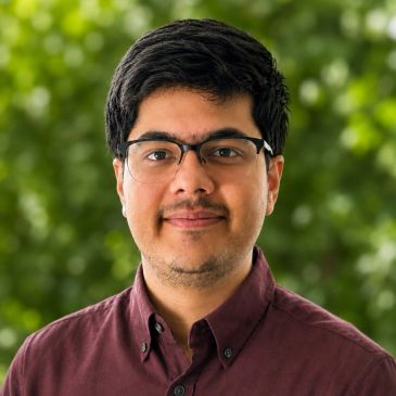 Portrait of a man wearing glasses and a maroon shirt.