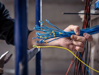 A male electrician works in a switchboard with an electrical connecting cable
