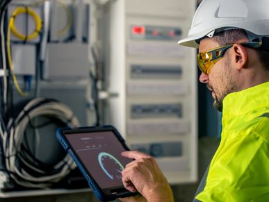 Man an electrical technician working in a switchboard with fuses uses a tablet
