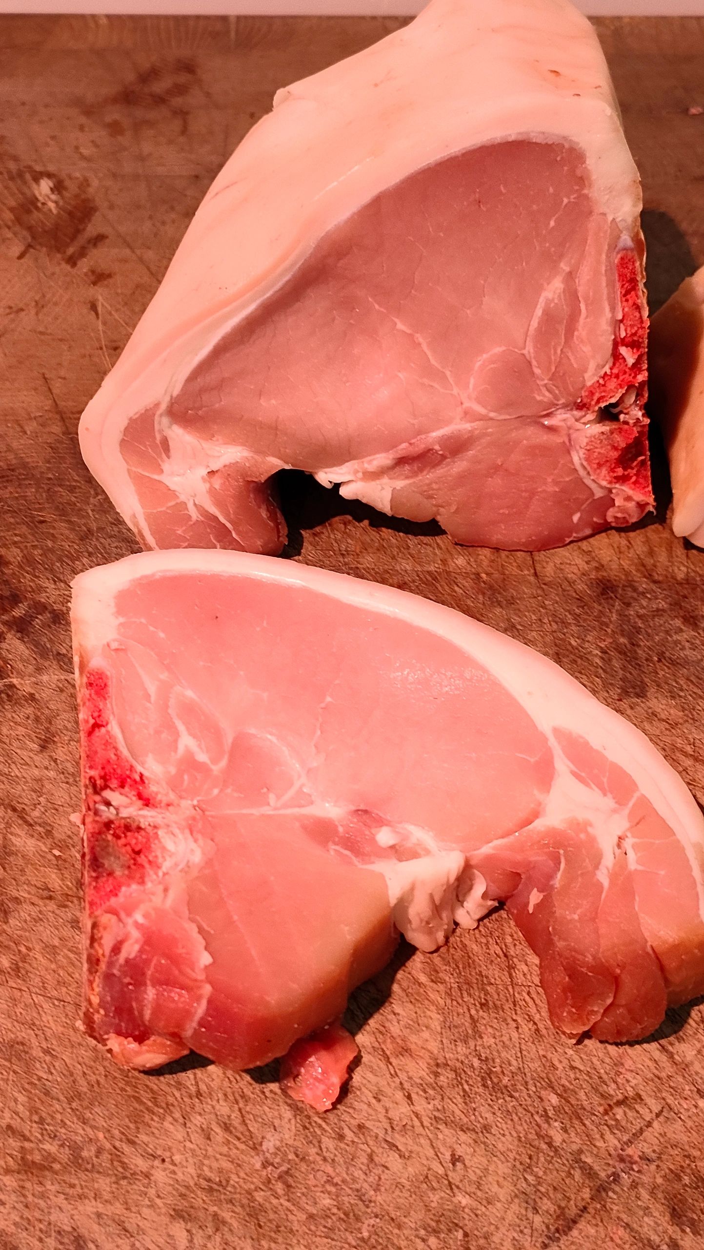 Two raw pork chops on a wooden cutting board.