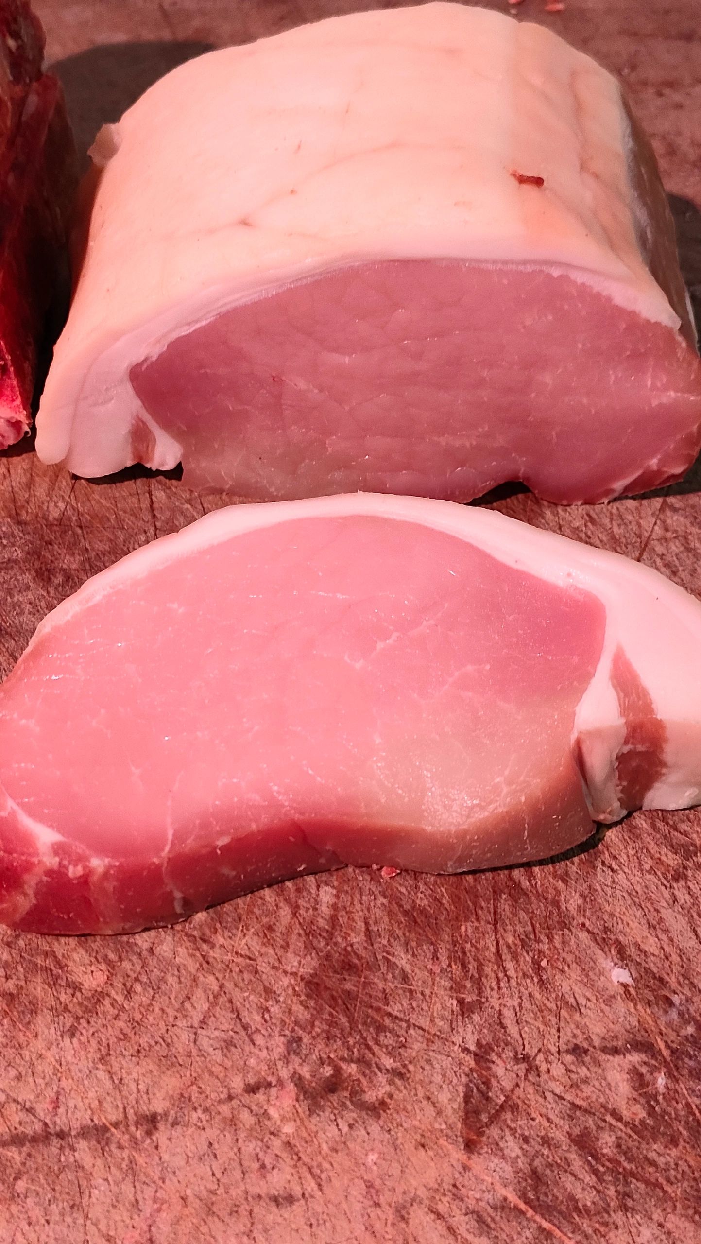 Two pieces of fresh raw pork with fat on a wooden cutting board.