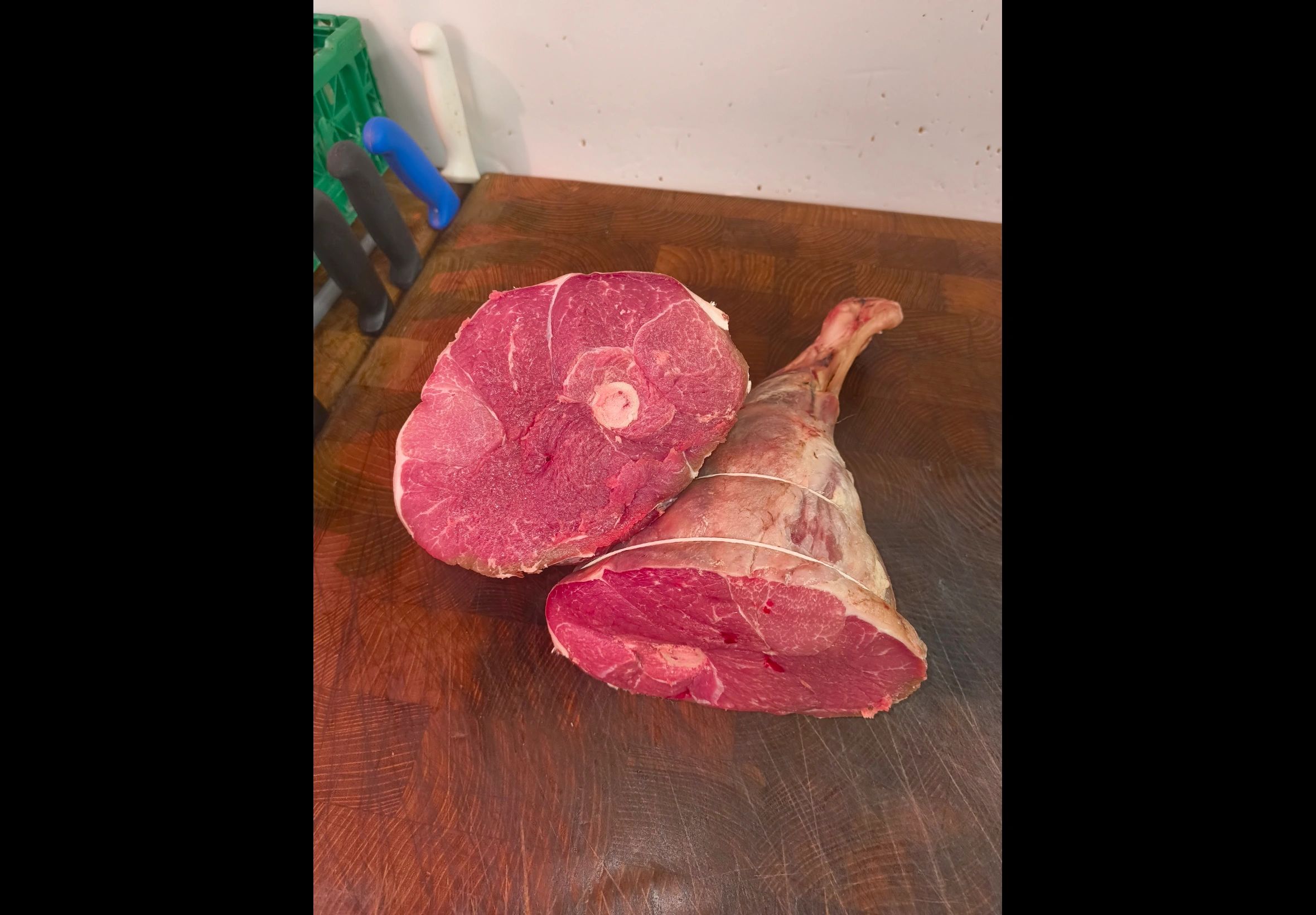 Fresh raw meat cuts on a wooden chopping board with knives in the background.