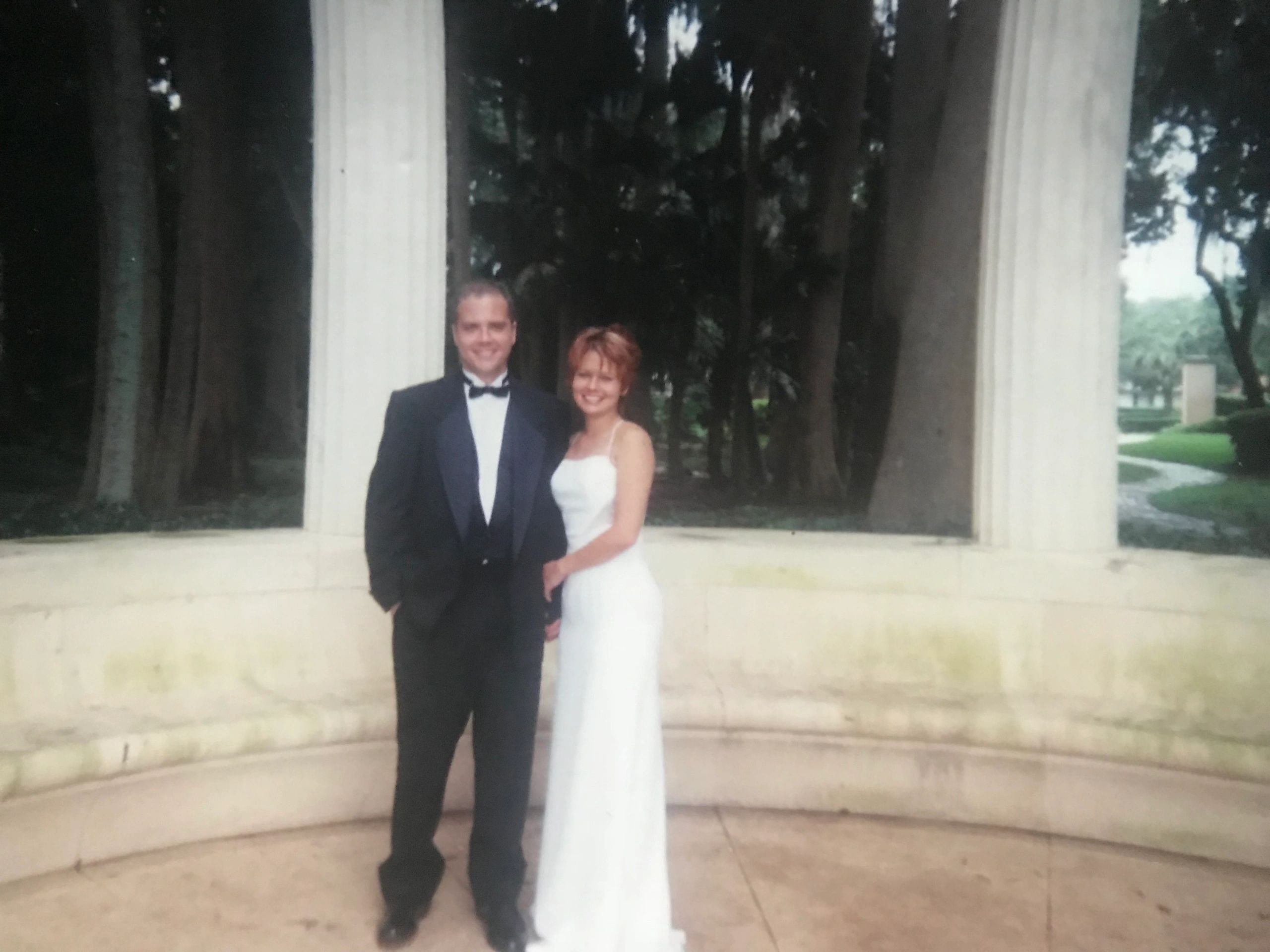 Couple dressed formally posing outdoors near columns.
