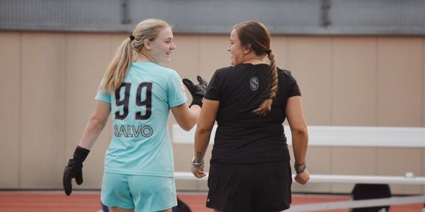 Two female athletes smiling and walking together on a sports field.