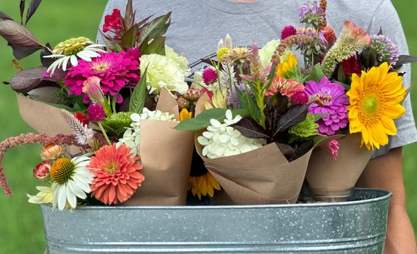 Person holding a metal bucket with colorful flower bouquets.