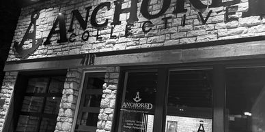 A photo taken of the outside of the Anchored Collective. Stone bricks and glass windows. 