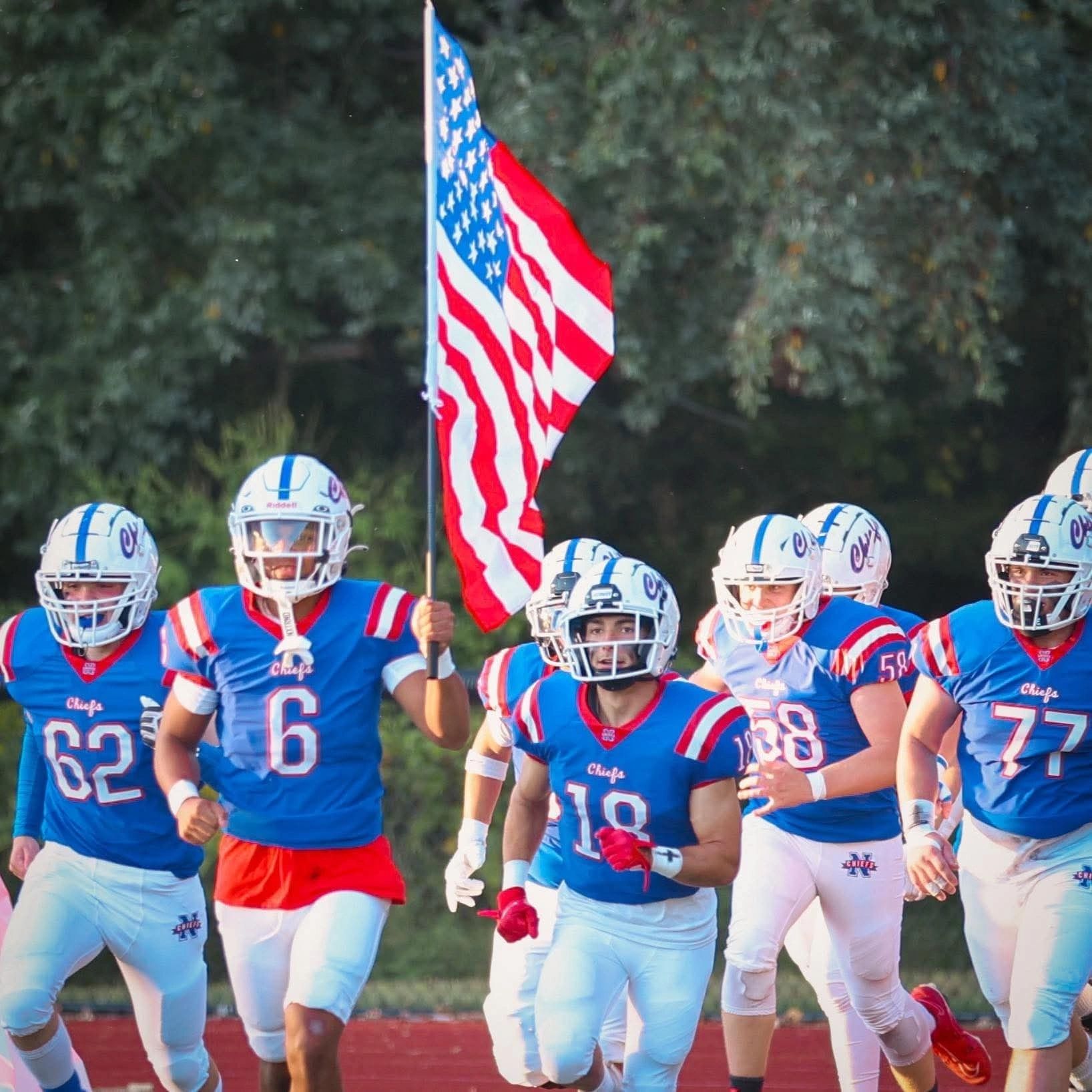 Football team running with an American flag.