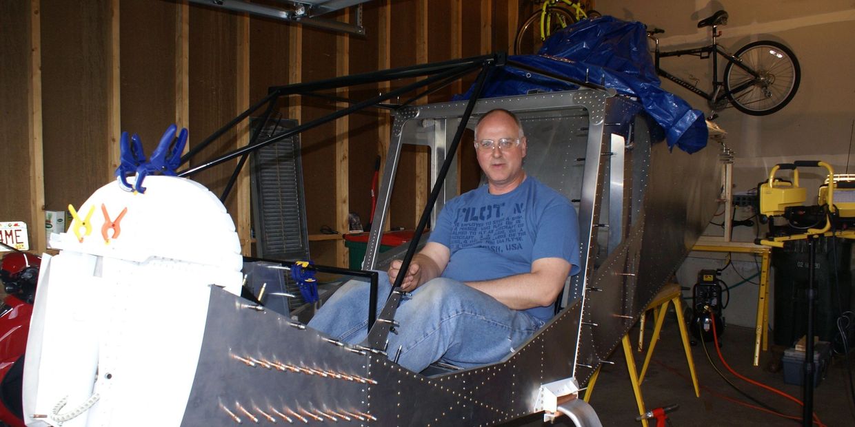 Man sitting inside an unfinished aircraft frame in a garage.