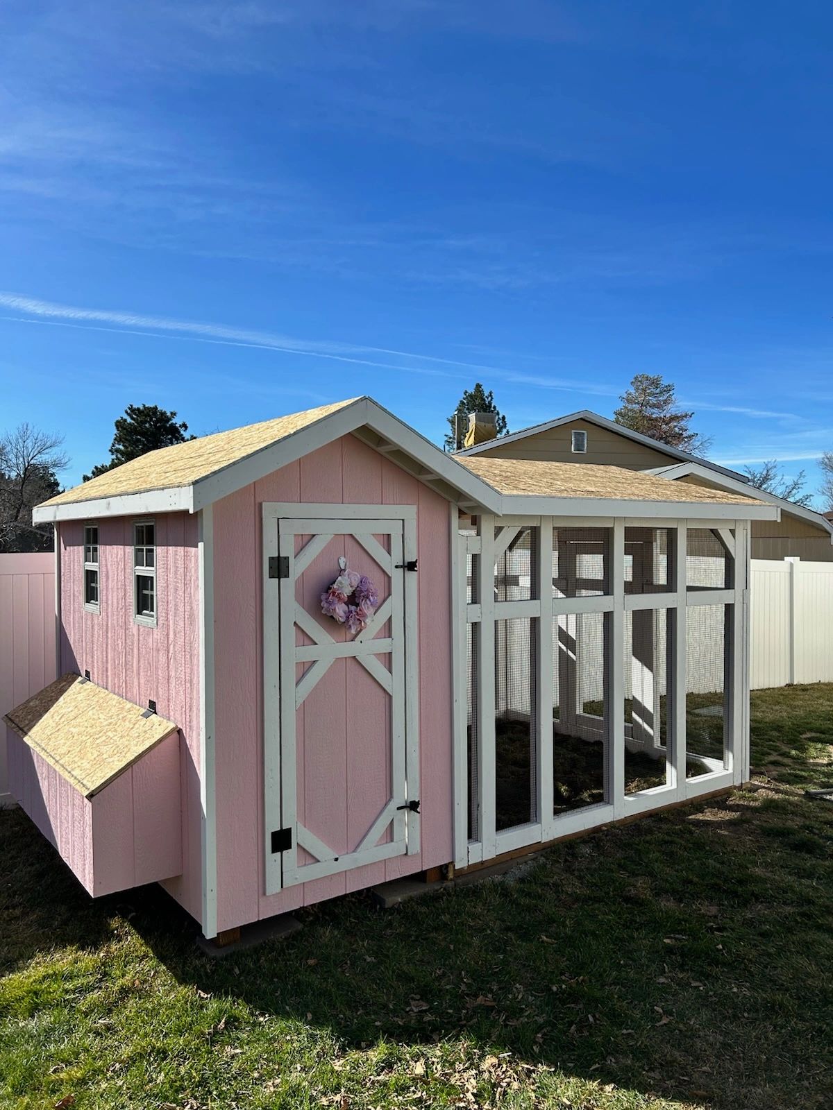 A pink and white chicken coop with a decorative flower wreath on the door.