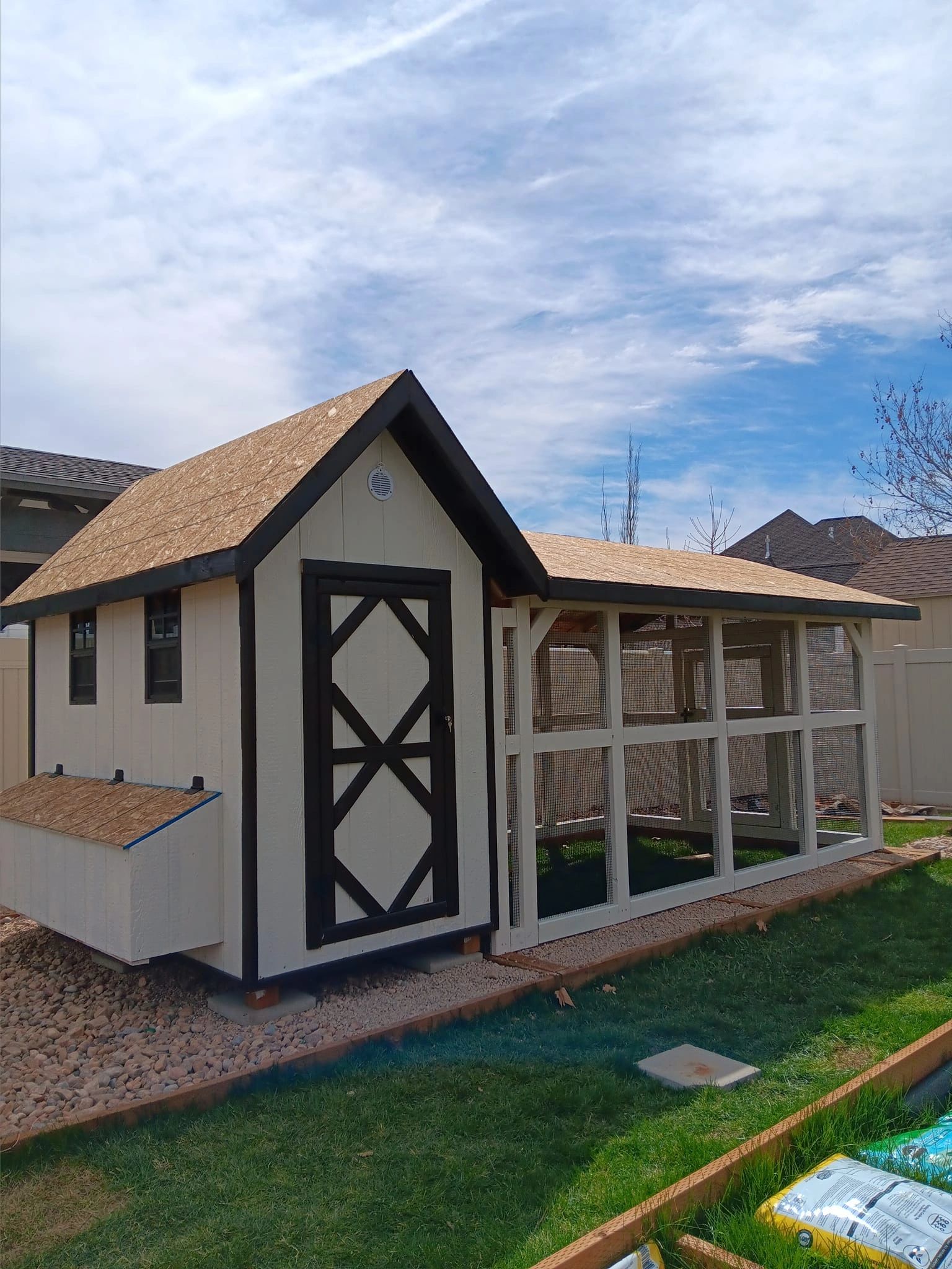 A large backyard chicken coop with fresh roofing under a partly cloudy sky.