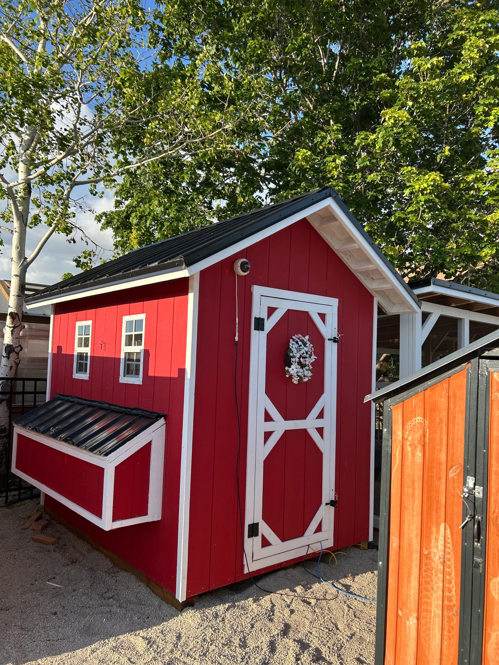 Small red and white chicken coop with a flower wreath on the door.