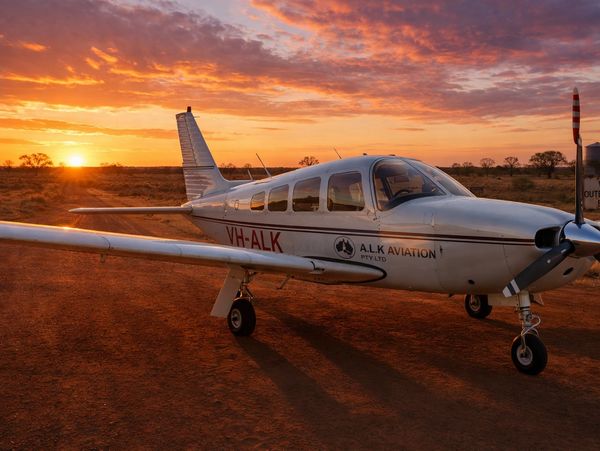 Small white airplane on red dirt at sunset with vibrant sky.