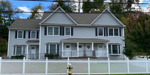 A symmetrical two-story white house with a white picket fence and a fire hydrant in front.