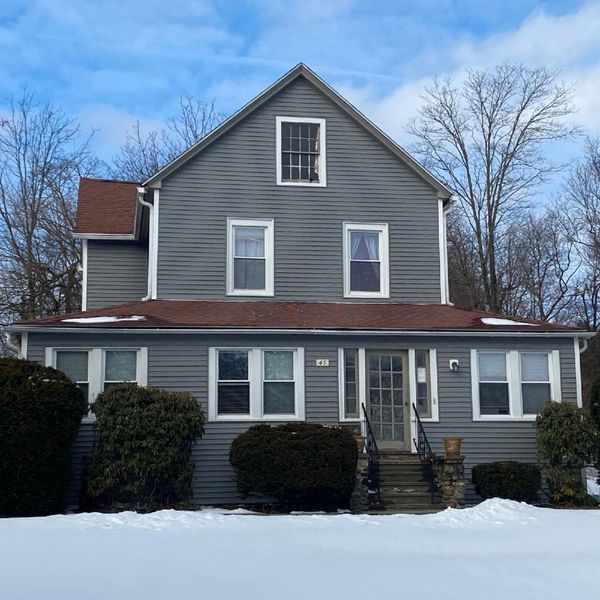A two-story gray house with a red roof surrounded by snow and leafless trees.