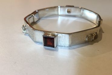 Custom bangle with garnets, moonstone and white topaz. Hinged with a friction fit closure.
One of a 