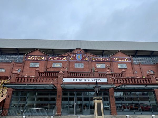 Photo of A large red brick building with the villa logo and Aston Villa sign, over the lower grounds