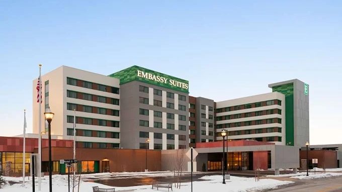 Modern Embassy Suites hotel building with snow on the ground at dusk.