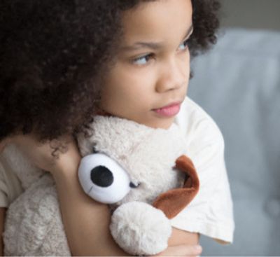 Child hugging a teddy bear, looking thoughtful.