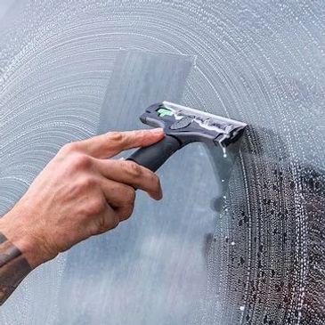 Man with tattoos cleaning a large window with a squeegee.