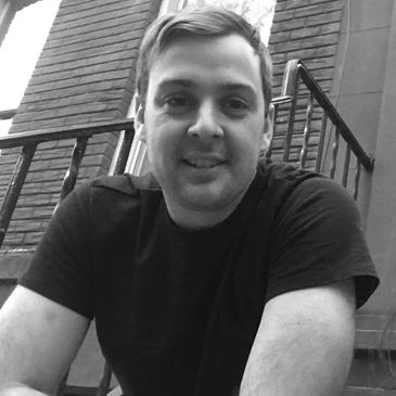 Man smiling outdoors near a staircase.