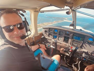 Man piloting a small aircraft with coastal view outside.