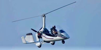 A person flying a gyrocopter against a clear blue sky.