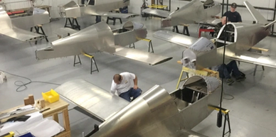 A workshop with several small, unfinished aircraft and workers assembling them.