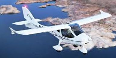 A white light aircraft flying over rocky terrain and water.