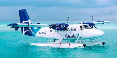 A blue and white seaplane floats on turquoise ocean water under a cloudy sky.