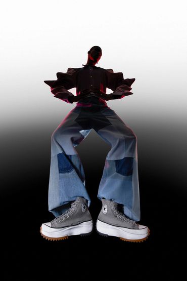 Model in patchwork jeans and platform Converse shoes against gradient background.