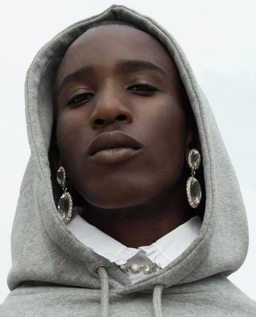 Close-up of a person wearing a grey hoodie and ornate dangling earrings.