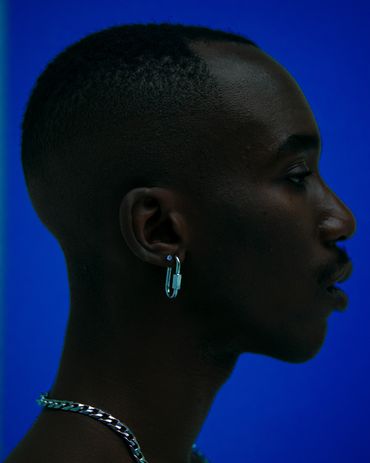 Profile of a man with silver jewelry against a bright blue background.