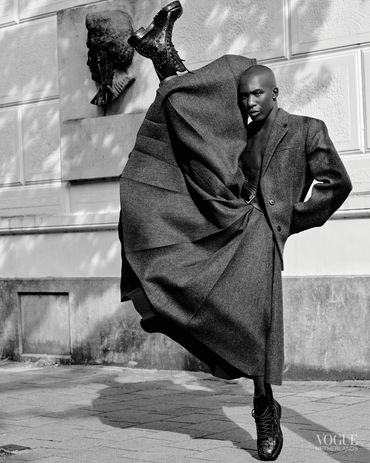 Fashion-forward model striking a dynamic pose in a flowing coat and combat boots.