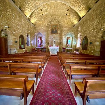 Interior of a stone-walled church with wooden pews and a red carpet aisle.