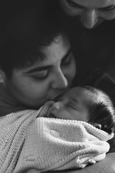 Two mothers kissing their newborn baby during a newborn photo session. 